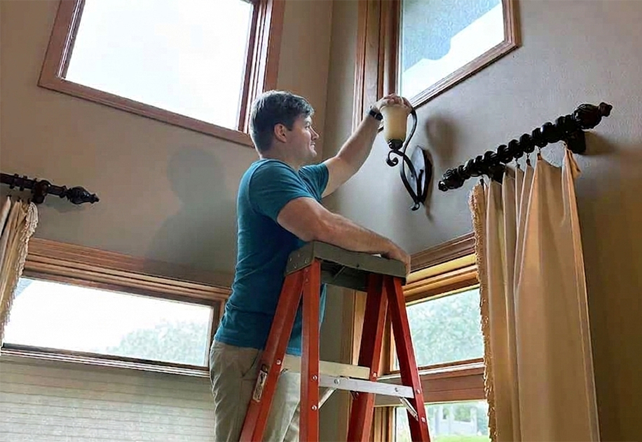 Worker changing light blub on ladder.